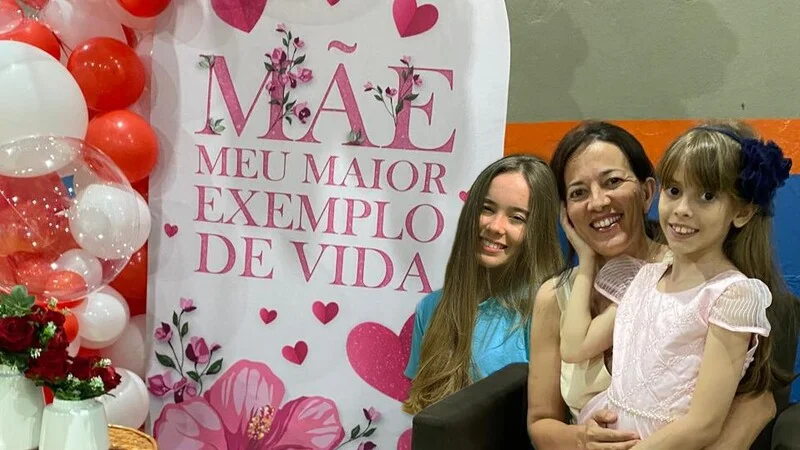 Viviane com as duas filhas em frente ao painel 'Mãe, meu maior exemplo de vida'